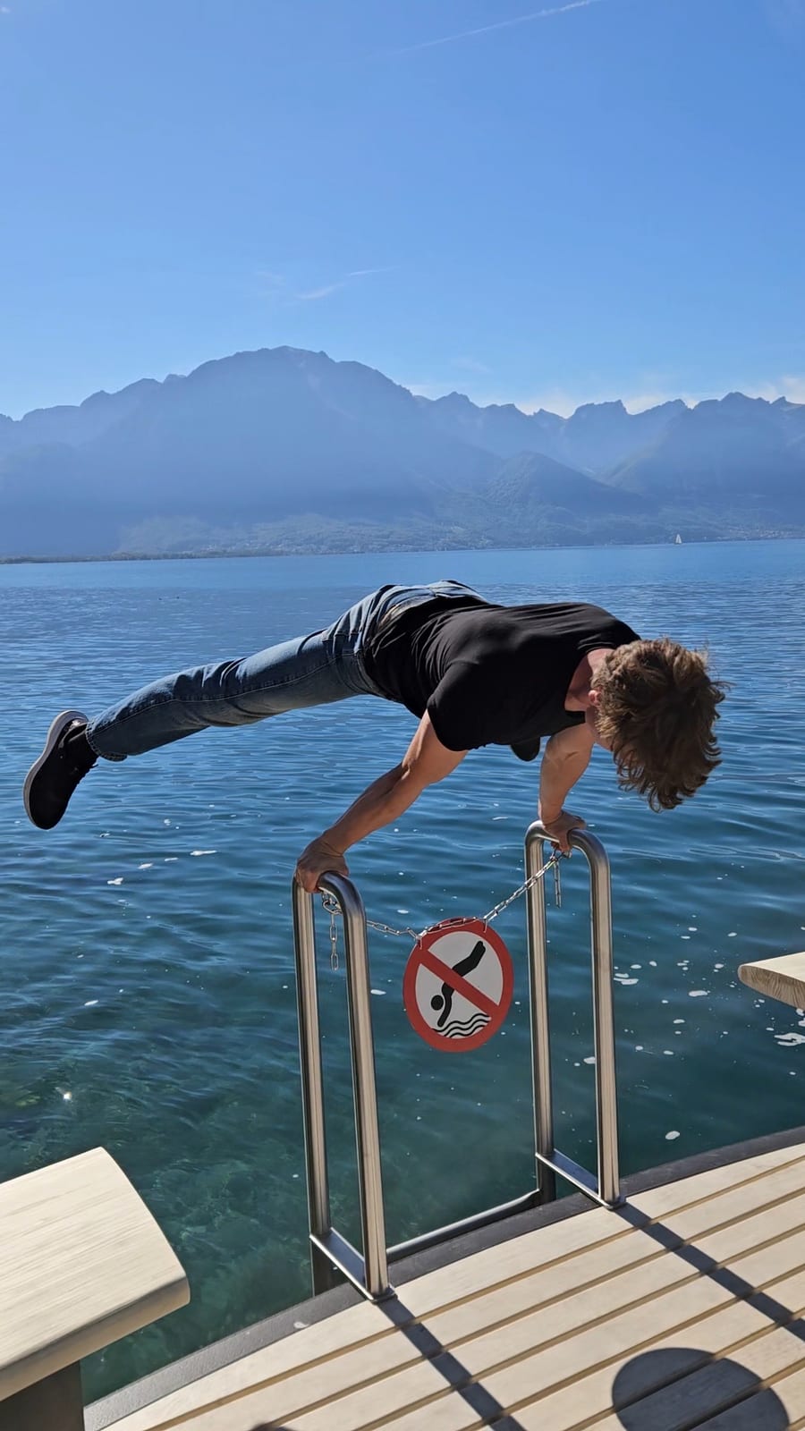 Walking green flag Richard Kocanda holding a planche on a lakeside railing with mountains behind him
