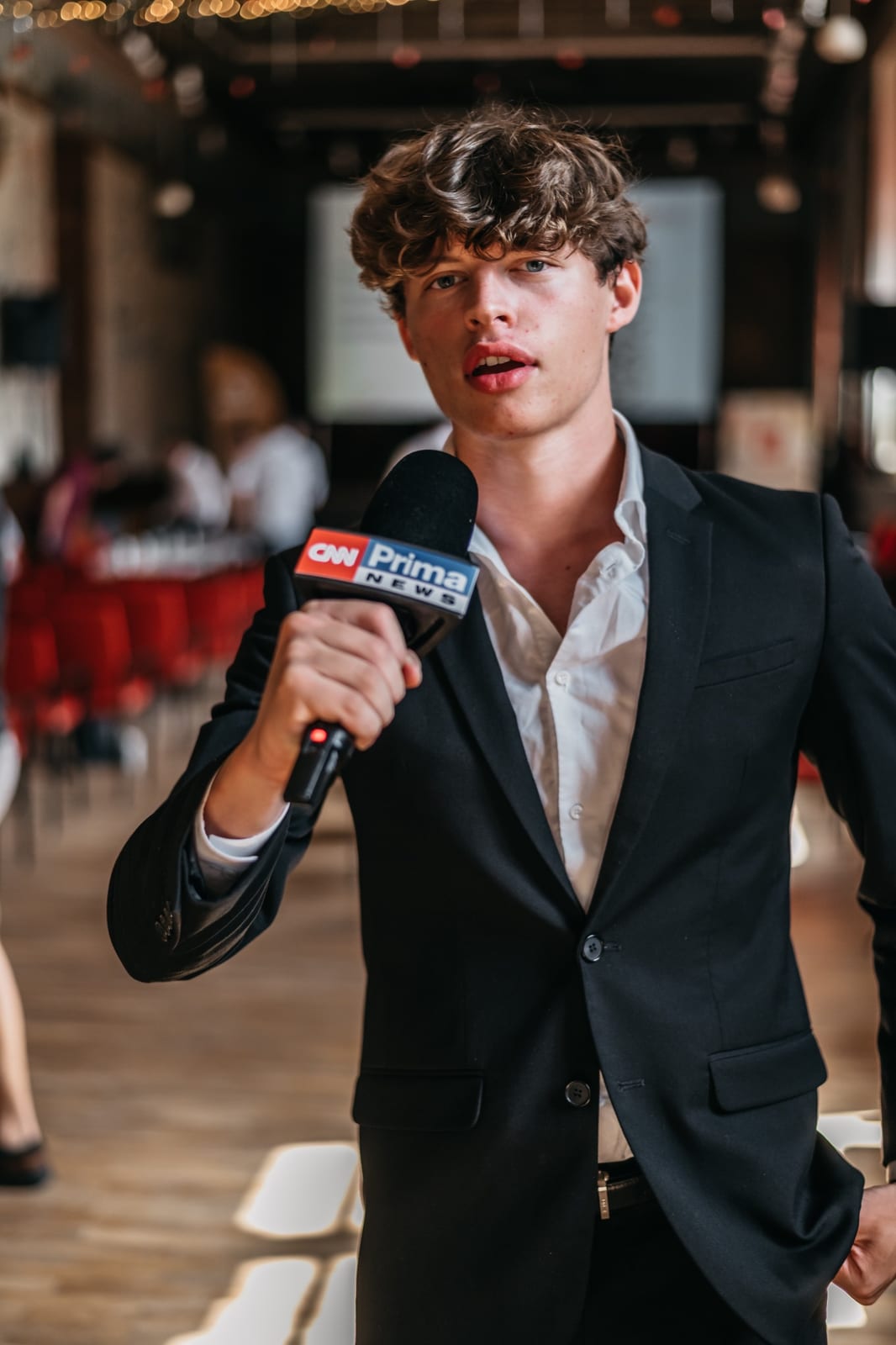 Richard Kocanda, a walking green flag, in a black suit holding a CNN Prima News microphone